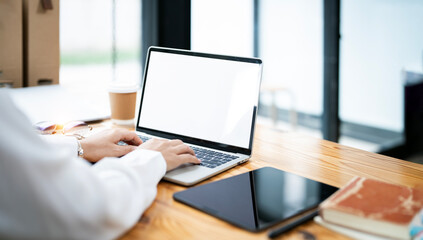 Fototapete - Businesswoman typing on a laptop with a blank screen at a desk in a well-lit co-workspace.