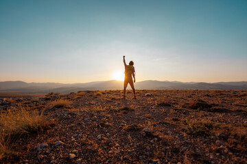 hiking in the mountains. a man with a backpack stands on a mountain against the backdrop of sunset. An active young man feels free.