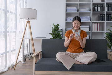 woman relaxes at home, reclining on the sofa with her smartphone, enjoying a peaceful moment of leisure and connection in her comfortable living space