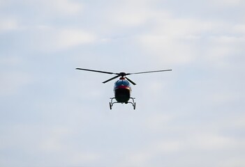 Helicopter flying through a clear blue sky with fluffy white clouds.