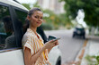 © SHOTPRIME STUDIO - Young woman using smartphone while leaning against car, urban background, soft focus, casual outfit, outdoor lifestyle concept, relaxed mood, summer vibes, modern city setting