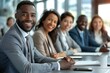 © Yuliia - group of diverse business people sitting at a desk in a modern office, smiling and engaged in a meeting or training session.