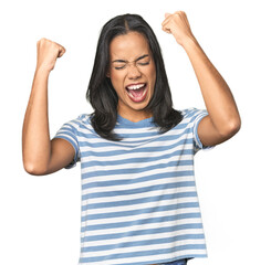 Wall Mural - young latina posing in studio raising fist after a victory, winner concept.