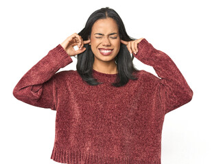 Wall Mural - simple portrait of a young latina covering ears with fingers, stressed and desperate by a loudly amb