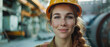 © AstraNova - close-up of smiling young caucasian woman engineer wearing yellow safety helmet looking forward in sweaty condition and working in open field factory background