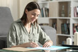 © PheelingsMedia - Happy woman reading and signing documents at home