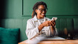 © (JLco) Julia Amaral - Black woman smiling while using smartphone in cafe