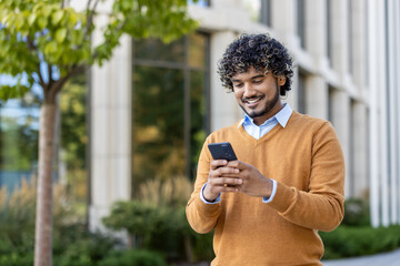 young professional with curly hair using smartphone outdoors. scene conveys connectivity, technology