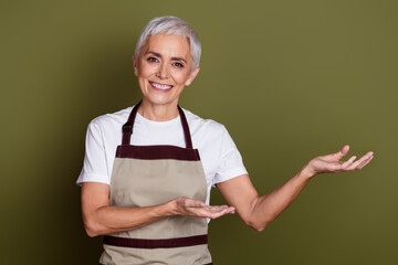 Sticker - Photo of cheerful pretty lady dressed apron owning cafe showing arms empty space isolated green color background