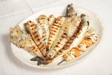 Mixed grill of fresh fish served on a large oval white restaurant plate.