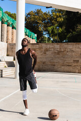 Wall Mural - Young african american basketball player in black t-shirt and shorts stretching on basketball court, sports concept, healthy movement