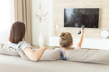 Mother and daughter sitting on sofa watching tv