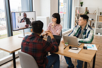 Wall Mural - Team engaged in video conference meeting, discussing business plans at modern office. Group of colleagues collaborating on project with virtual participant.