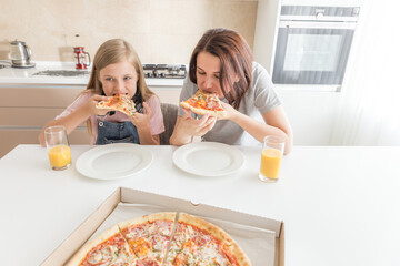 Mother and daughter sitting in the kitchen, eating pizza and having fun. Focus on daughter