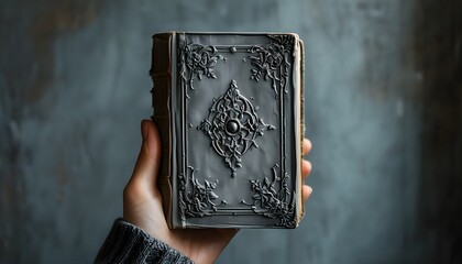 Wall Mural - Hand gripping a grey-covered book against a neutral background