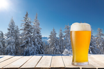 Wall Mural - glass of beer on wooden table against winter landscape