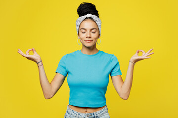 Wall Mural - Young spiritual Latin woman she wears blue top t-shirt headband casual clothes hold hands in yoga om aum gesture relax meditate try to calm down isolated on plain yellow background. Lifestyle concept.