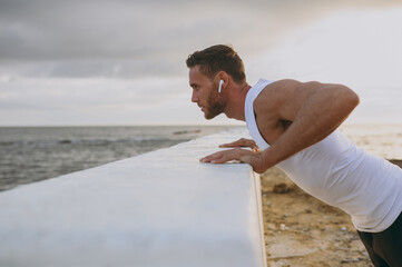 Wall Mural - Side view young strong athletic toned fit sportsman man wear sports clothes earphones do supported push-up warm up training at sunrise sun dawn over sea beach outdoor on seaside in summer day morning.