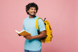 © ViDi Studio - Side view young smart reader Indian boy student in blue t-shirt casual clothes backpack bag hold read book look aside on area isolated on plain pink background High school university college concept