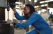© KANGWANS - A man in a blue jumpsuit is working on a machine. He is wearing gloves and a watch