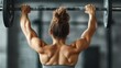 © Maximages  - An athletic woman seen from the back, lifting a barbell as part of a shoulder press workout in a gym. The image captures strength and muscle definition during exercise.