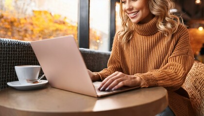 Smiling woman working on laptop in cozy cafe with coffee, daytime, casual autumn attire, productivity and relaxation concept