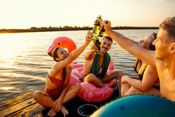 Wall Mural - Group of friends in swimsuit having fun sitting on a pier drinking beer enjoying a summer day at the lake.