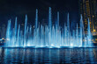 © Kitta - Dubai Mall fountain show at night features stunning water jets illuminated in blue, creating mesmerizing display against city skyline