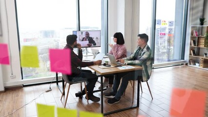 Wall Mural - Team video conference meeting in modern office with participants applauding virtual presenter. Colleagues gathered around table with laptops, taking notes, and engaging in discussion.