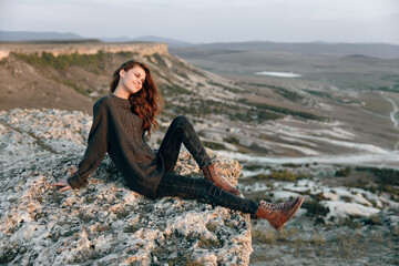 Wall Mural - Serene woman sitting on rocky ledge with panoramic view of valley and mountains in background