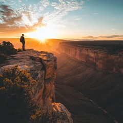 Poster - Silhouette of a hiker standing on a cliff overlooking a canyon during a sunset.