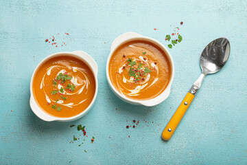 Creamy pumpkin soup bowls on blue background with parsley and pink pepper, a cozy autumn meal option