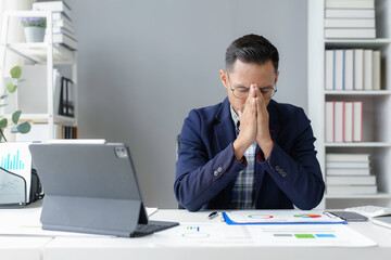 Wall Mural - Stressed asian businessman suffering headache at workplace