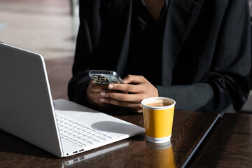 Closeup of hands using a smartphone while working with a laptop in a coffee shop