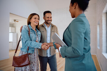 Wall Mural - Happy woman shaking hands with real estate agent while buying new apartment with her husband.