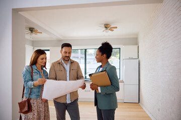 Happy African American real estate agent and her clients analyzing blueprints of  new house.