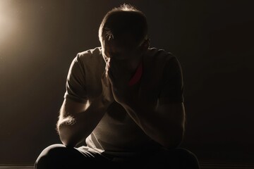 Religious young man praying to God on dark background, black and white effect Religious young man praying to God on dark background, black and white effect