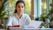 © Elshad Karimov - A woman sits at a table with a red stapler and a stack of paper. She is wearing a white shirt and has dark hair pulled back in a ponytail. She is looking at the camera with a neutral expression.
