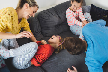 A family enjoying a cozy moment on the couch, watching TV. Two young girls, one with glasses, are smiling and laughing, while a man, presumably their father, looks surprised or amused. A dog is comfor