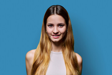 Wall Mural - Portrait of beautiful young girl with long red hair looking at camera on blue background