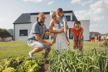 a family gardening together in a backyard. two adults and two children are tending to plants, with a