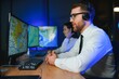 © Serhii - In Monitoring Room Technical Support Specialist Speaks into Headset. His Colleagues are Working in the Background