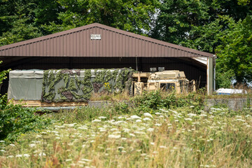 unloaded British army MAN HX77 8x8 EPLS Heavy Utility Truck in front of a large open fronted barn