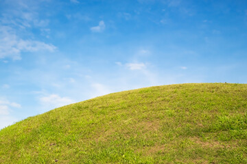 Lush green grass hill under a bright blue sky with scattered white clouds.