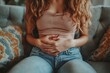 © itchaznong - A woman with a stomach ache is sitting on a couch