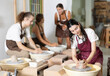 © JackF - Positive young lady wearing apron modeling clay dish from row material using pottery wheel in taller workroom