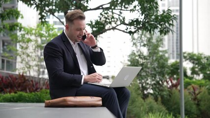 Wall Mural - Caucasian businessman sitting at eco park while talking by using phone and working on laptop. Professional executive manager explain marketing idea from computer while calling to investor. Urbane