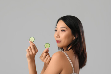 Wall Mural - Beautiful Asian woman with cucumber slices on grey background