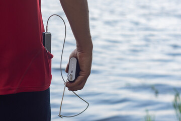 A man charges a smartphone with a power bank. The phone in hand is being charged with a portable charger against the backdrop of the lake.