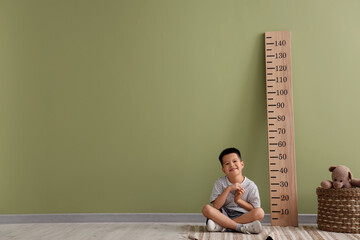 Little Asian boy with stadiometer near green wall